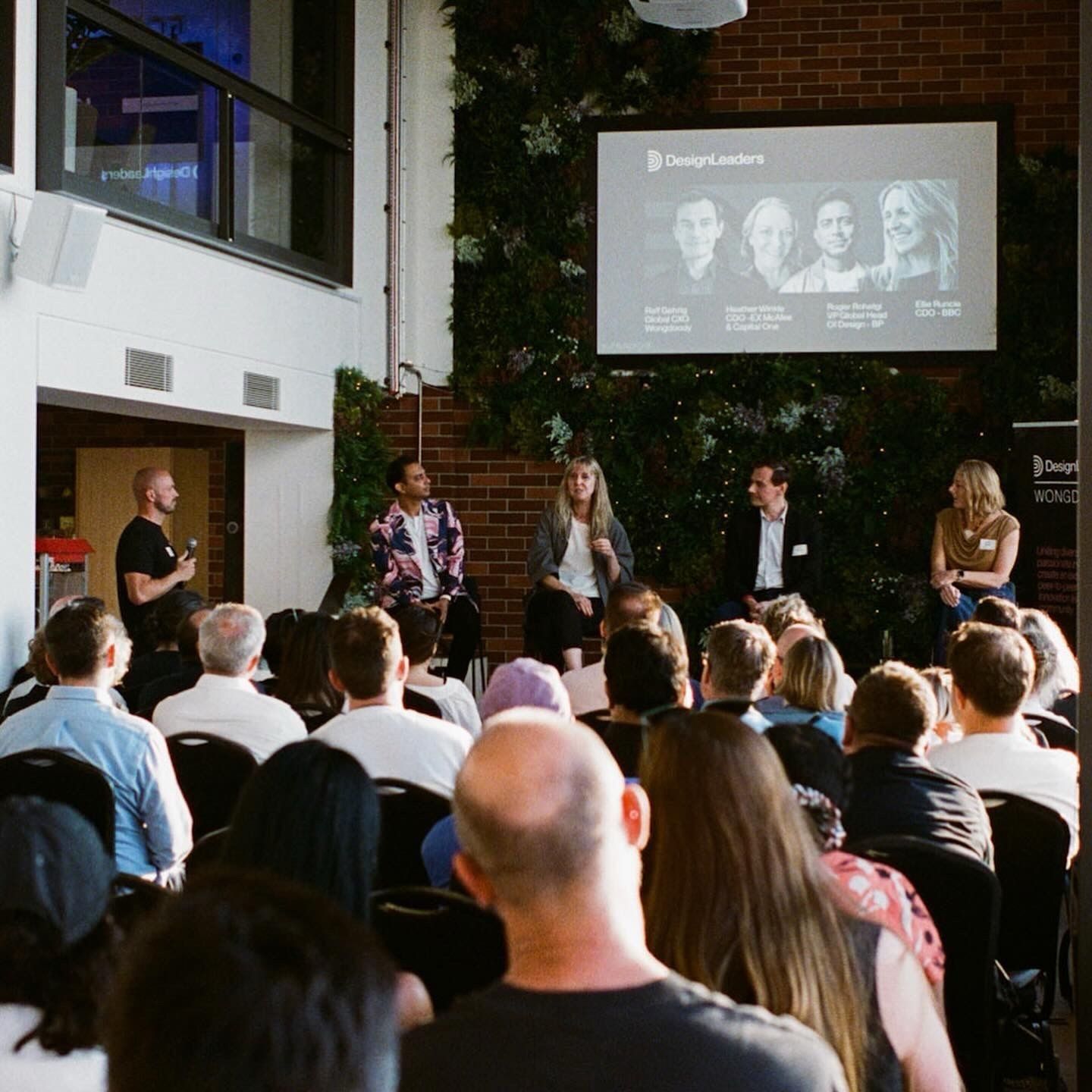 Members facing a panel and the Design Leaders screen